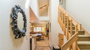 A spacious hallway with a wooden staircase leading to an upper floor. A decorative mirror hangs on the wall, and a dining area is visible in the background.