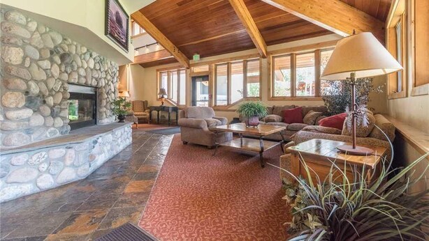 A spacious living room with a stone fireplace, wooden beams, large windows, and comfortable seating.