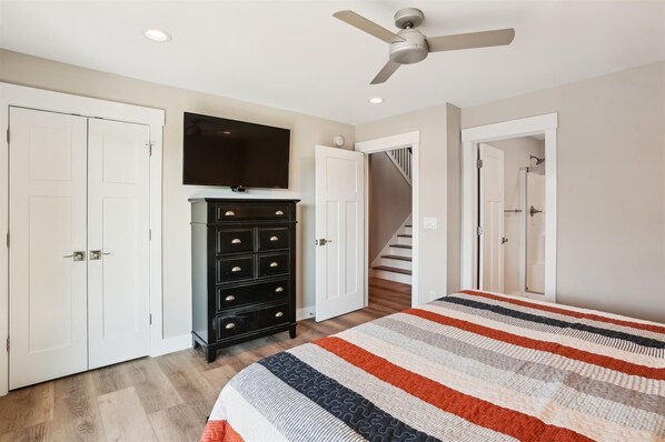 Une chambre à coucher avec un lit, une commode, un téléviseur et un escalier.