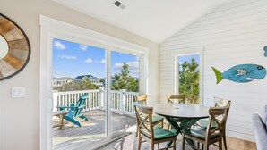 En balkon med et bord og stole, havudsigt og et maleri af fisk på væggen.