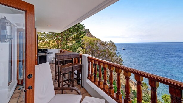 Un balcon avec vue sur la mer, un barbecue, des meubles en osier et une rambarde en bois.