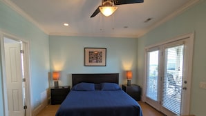 A bedroom with a bed, two bedside lamps, a ceiling fan, a framed picture on the wall, and a window with blinds. - Fabulous views  - right across the street from the beach! (Carolina Beach)
