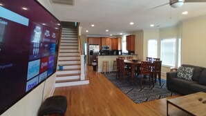 A spacious living room with a flat-screen TV, a staircase leading to a kitchen, and a dining area with wooden furniture. - Fabulous views  - right across the street from the beach! (Carolina Beach)