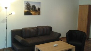 A living room with a sofa, a small table, a lamp, and a cabinet. - Apartment Berger - Apartment (Timmendorfer Strand)