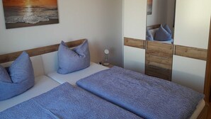 A bedroom with two beds, a wooden headboard, a bedside table with a lamp, and a large wardrobe with a mirror. - Apartment Berger - Apartment (Timmendorfer Strand)