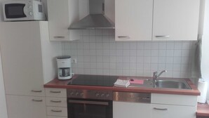 A compact kitchen with white cabinets, a microwave, a coffee maker, a sink, and a dishwasher. - Apartment Berger - Apartment (Timmendorfer Strand)