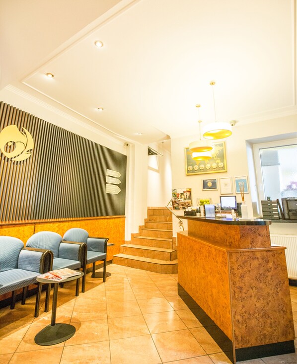 A reception area with a reception desk, a staircase, and seating with a magazine on the floor. - BARDOLINO Fine.Food.Hotel (Nuremberg)