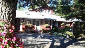 A two-story building with a red facade, a covered porch, and a variety of potted plants and flowers in the front yard. - Super Clean, Fully-Equipped Private Suite 1 Mile from Acadia (Bar Harbor)