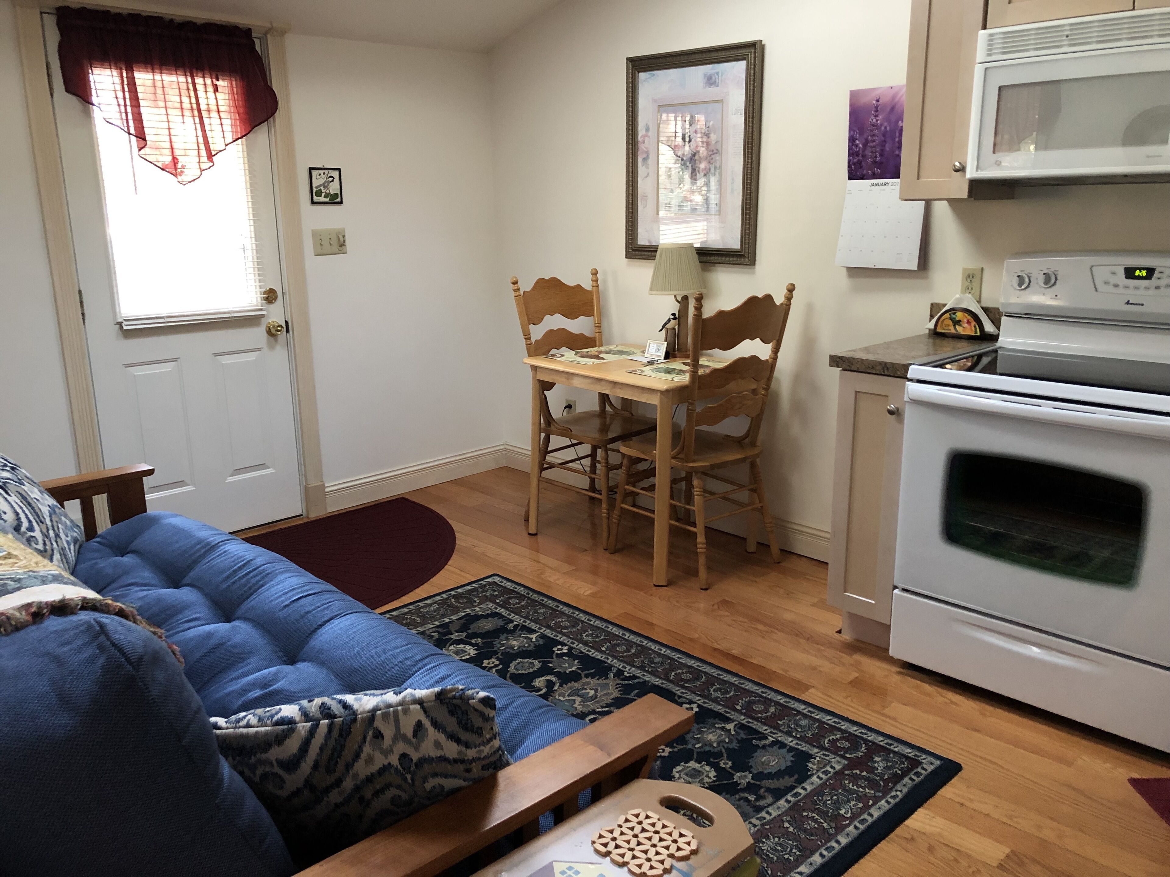 A living room with a blue sofa, a wooden dining table with chairs, a kitchen with a stove and microwave, and a door with a window.