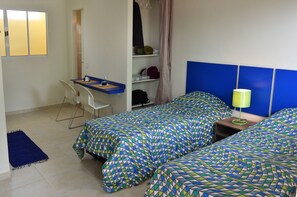 A small, neatly arranged bedroom with two single beds, a desk with a chair, a wardrobe, and a bedside table with a lamp. - Studio Ana Laura (São Paulo)