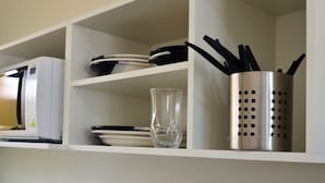 A kitchen shelf with a microwave, plates, a glass, and a utensil holder. - Studio Ana Laura (São Paulo)