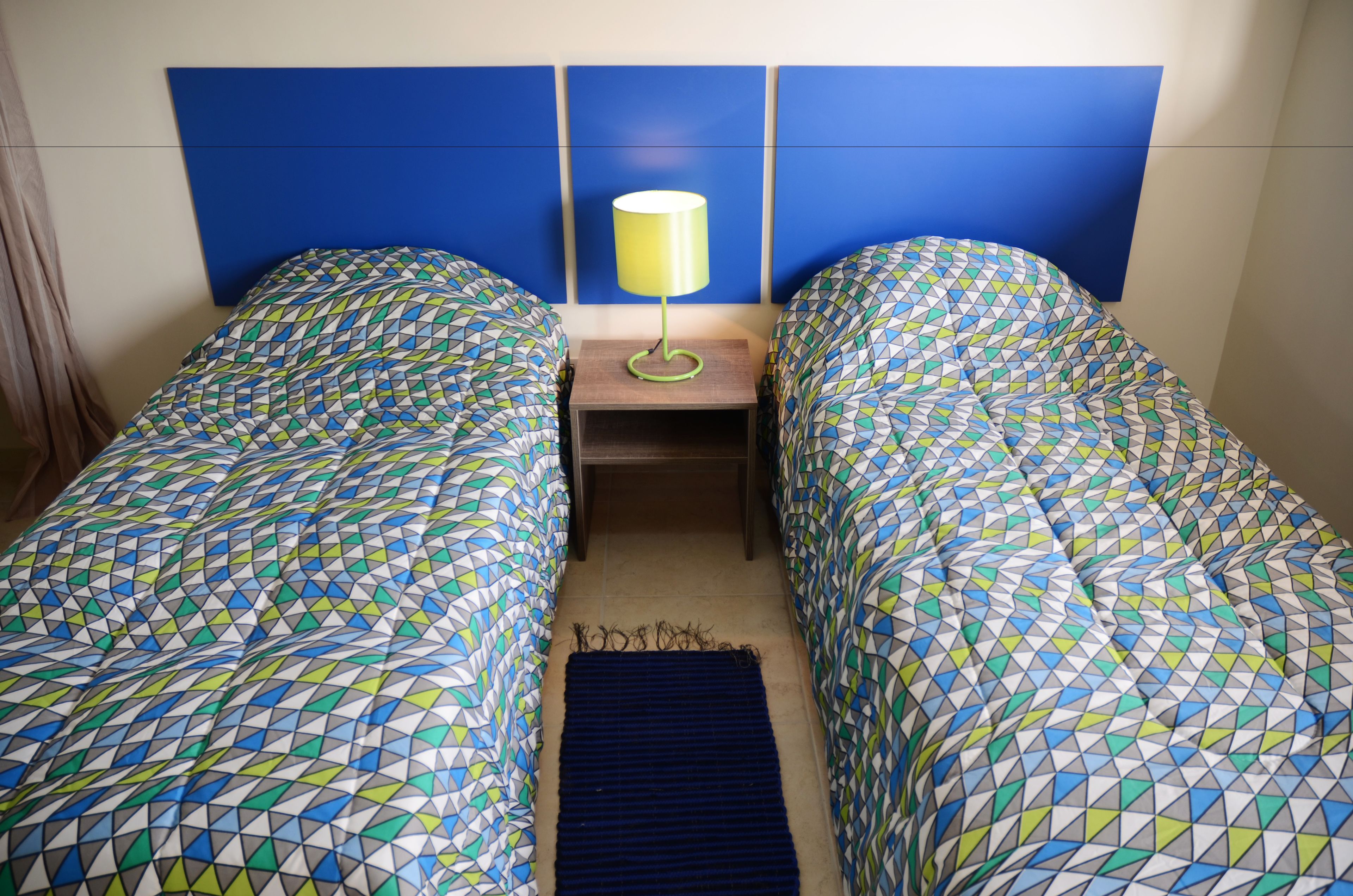 A twin room with two beds, a nightstand with a lamp, and a blue headboard.