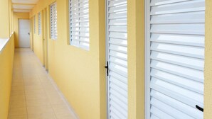 A long corridor with closed white shutters, yellow walls, and a tiled floor. - Studio Ana Laura (São Paulo)