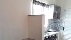 A compact kitchen with a dining area, a tiled backsplash, and a small window with curtains. - Studio Ana Laura (São Paulo)