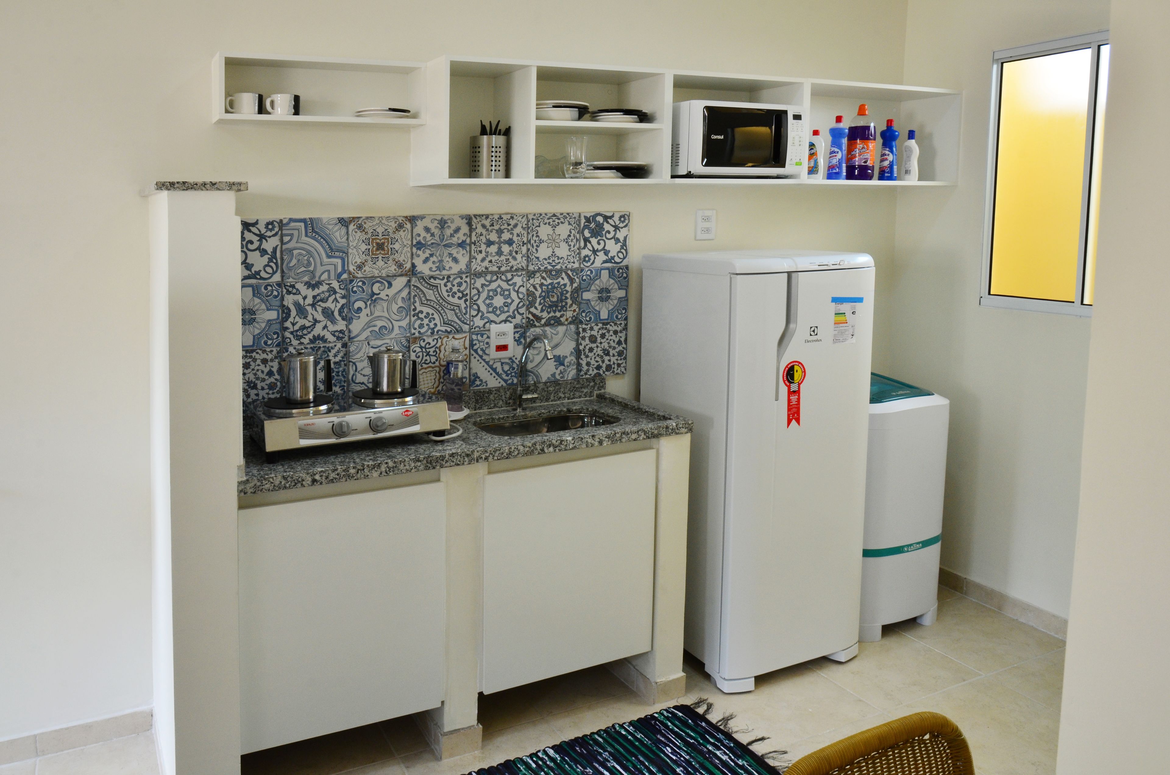 Cocina compacta con estufa, lavamanos y refrigerador, que presenta un salpicadero con diseño y armarios blancos.