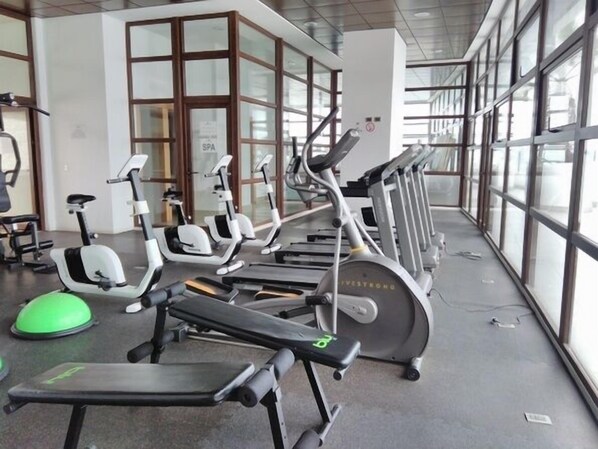 Un gimnasio con diverso equipo de ejercicio, incluyendo cintas de correr y bicicletas estáticas, dispuestos en fila.