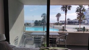 A hotel room with a bed, a table, and chairs. There is a view of a pool and palm trees outside. - Depto Jardín del Mar La serena 941 (Coquimbo)