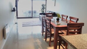 A modern dining area with a glass table and wooden chairs, a sofa, and a sliding glass door leading to an outdoor seating area. - Depto Jardín del Mar La serena 941 (Coquimbo)