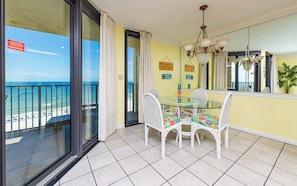Un balcón con puerta de vidrio, una mesa de comedor con sillas y vista a la playa.