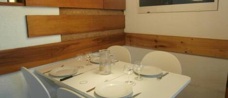 Un comedor con una mesa dispuesta para cuatro personas, sillas blancas y un cuadro en la pared.