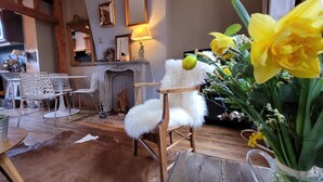 A cozy living room with a fireplace, white furry chair, and a vase of yellow flowers.