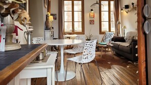 A cozy living room with a round dining table, white chairs, a sofa, and a wooden floor.