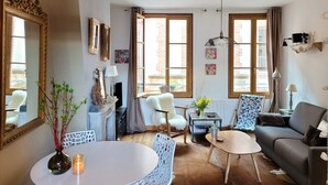 A cozy living room with a fireplace, a dining table with chairs, a sofa, and a large mirror.