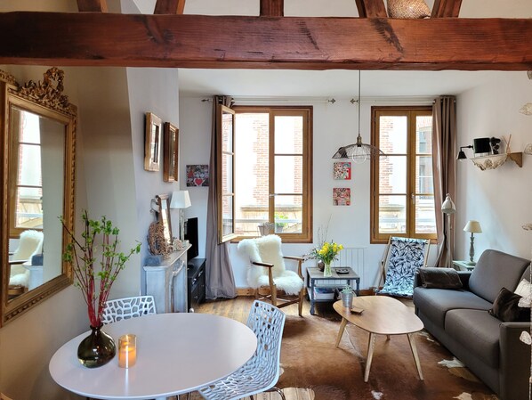 A cozy living room with a fireplace, a dining table with chairs, a sofa, and a large mirror.