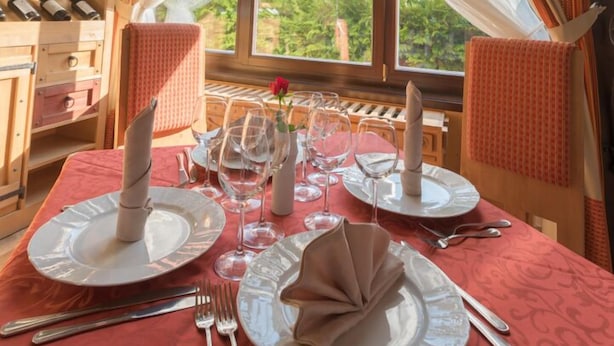 Mesa de comedor lista para cuatro, con copas de vino, platos y cubiertos.