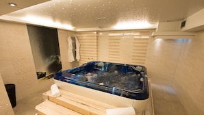 Un moderno spa con una amplia bañera de hidromasaje azul, bancos de madera y suelo de baldosas.