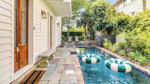 A swimming pool with two green and white inflatable rings, a stone-tiled deck, and a door with a brass handle.