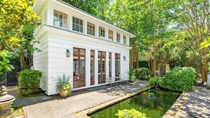 A white two-story building with a small garden and a pond.
