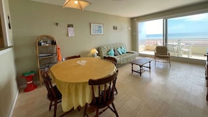 Een ruime woonkamer met een ronde eettafel, een bank en een balkon met uitzicht op zee.