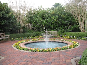 A circular brick fountain surrounded by flower beds and benches in a landscaped garden.