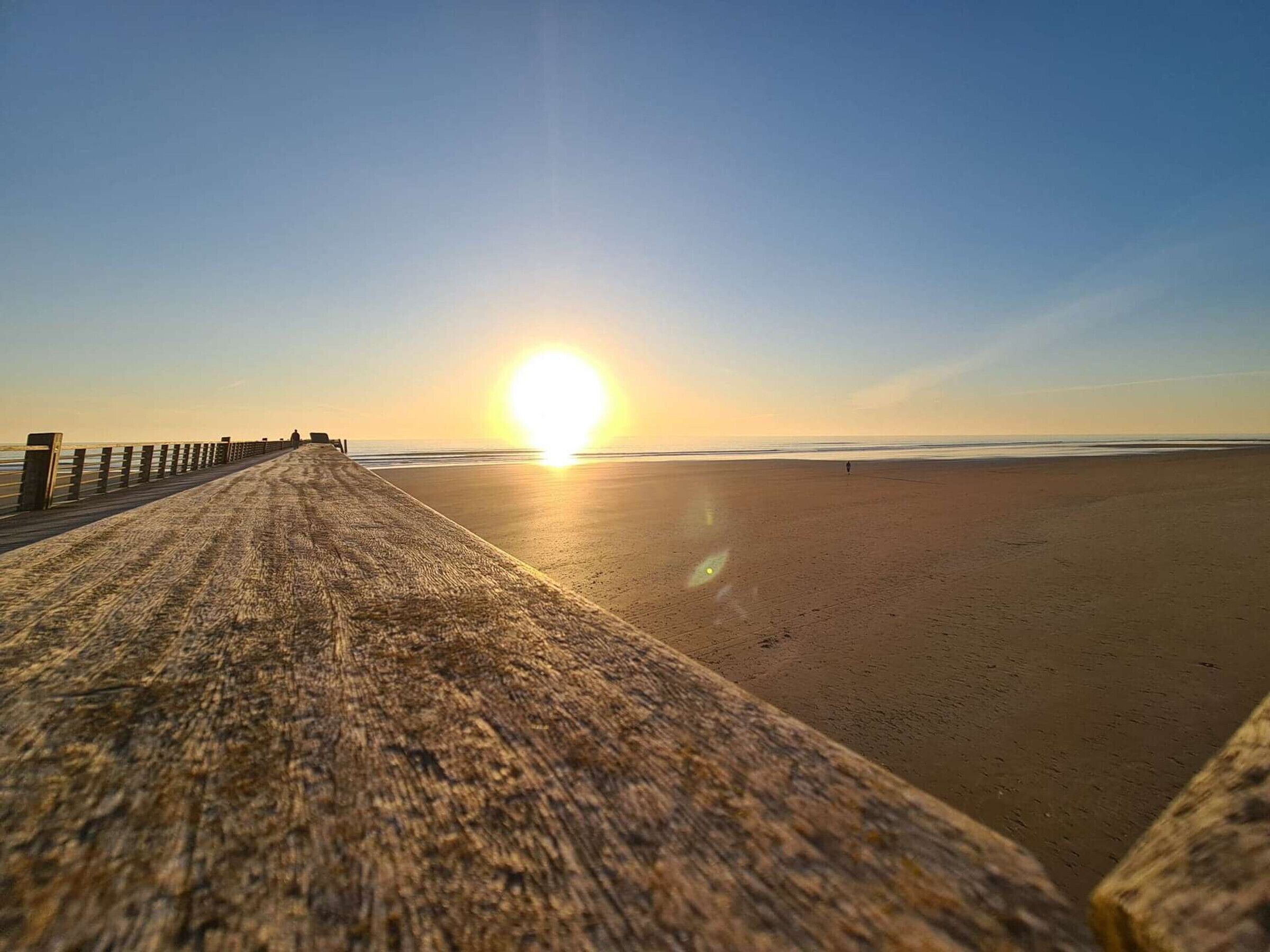 Una pasarela de madera que lleva a una playa con el sol poniéndose en la distancia.