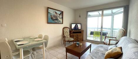 A living room with a dining area, a television, and a large window with a view.