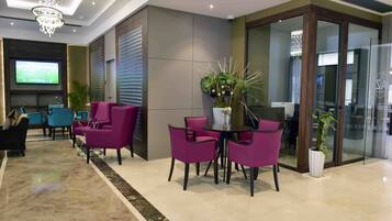 A modern lobby with a large TV screen, purple and blue chairs, a chandelier, and a potted plant.
