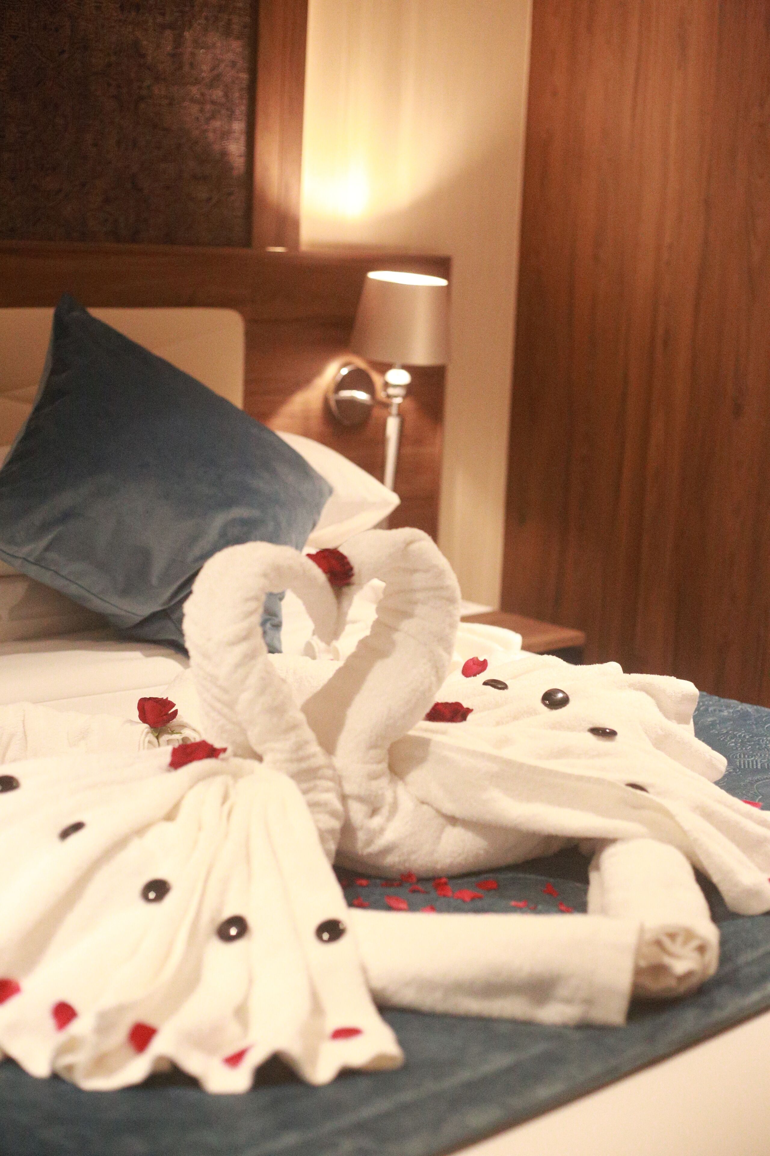 A bed with a blue pillow, white towels, and red rose petals.