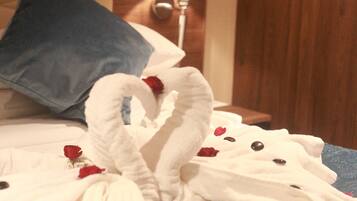 A bed with a blue pillow, white towels, and red rose petals.