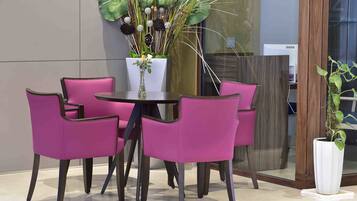 Een moderne binnensetting met een ronde tafel, omringd door vier paarse stoelen, een witte vaas met bloemen en een grote potplant met brede bladeren.