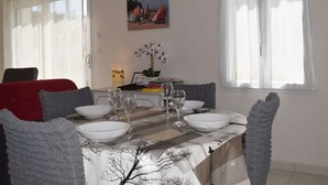 A dining area with a table set for four, a painting on the wall, and a window with curtains.