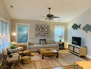 Uma sala de estar com sofá, mesa de centro, televisão e objetos decorativos.