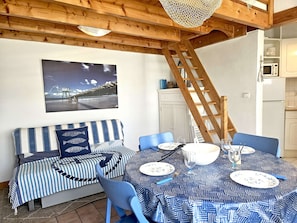 A dining area with a table set for four, a blue-striped sofa, and a wooden ladder.