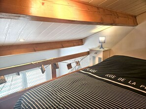A bedroom with a bed, a nightstand, a lamp, a window with a view, and a wooden ceiling.