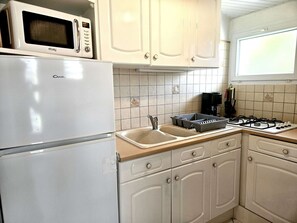 Una cuina amb nevera blanca, microones, fogó de gas i un rentaplat.