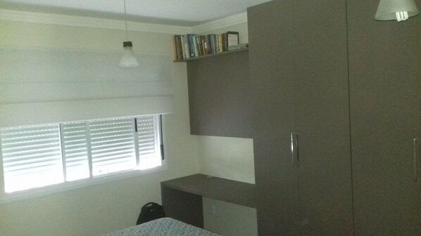 A room with a window, a desk, a wardrobe, and a shelf with books.