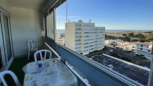 A balcony with a table and chairs, overlooking a coastal area with buildings and a clear sky.