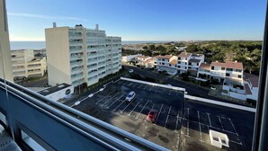 A high-rise building with multiple floors, a parking lot with several cars, and a view of the sea and surrounding buildings.