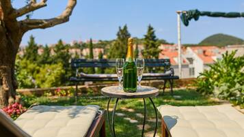 A garden setting with a table holding a bottle and glasses, a bench, and lounge chairs.