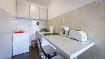 A compact kitchen with white cabinets, a small refrigerator, a toaster, and a kettle.